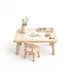 A child-sized table set for a project: a jar of paintbrushes, a paint palette, a pressed-leaf study part-finished on paper, a lump of clay and a pine cone, with one small chair pulled up