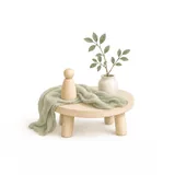 A small round wooden table with a simple peg doll, a length of green play silk draped over the edge and a stoneware jar holding a leafy branch